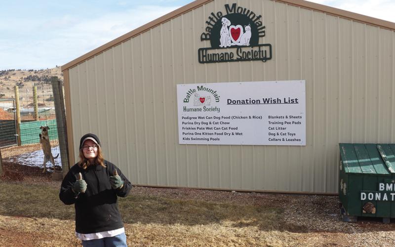 Proud employee Chloe Smith poses in front of a sign at Battle Mountain Humane Society which lists the facility’s Donation Wish List. Photo by Brett Nachtigall/Fall River County Herald-Star
